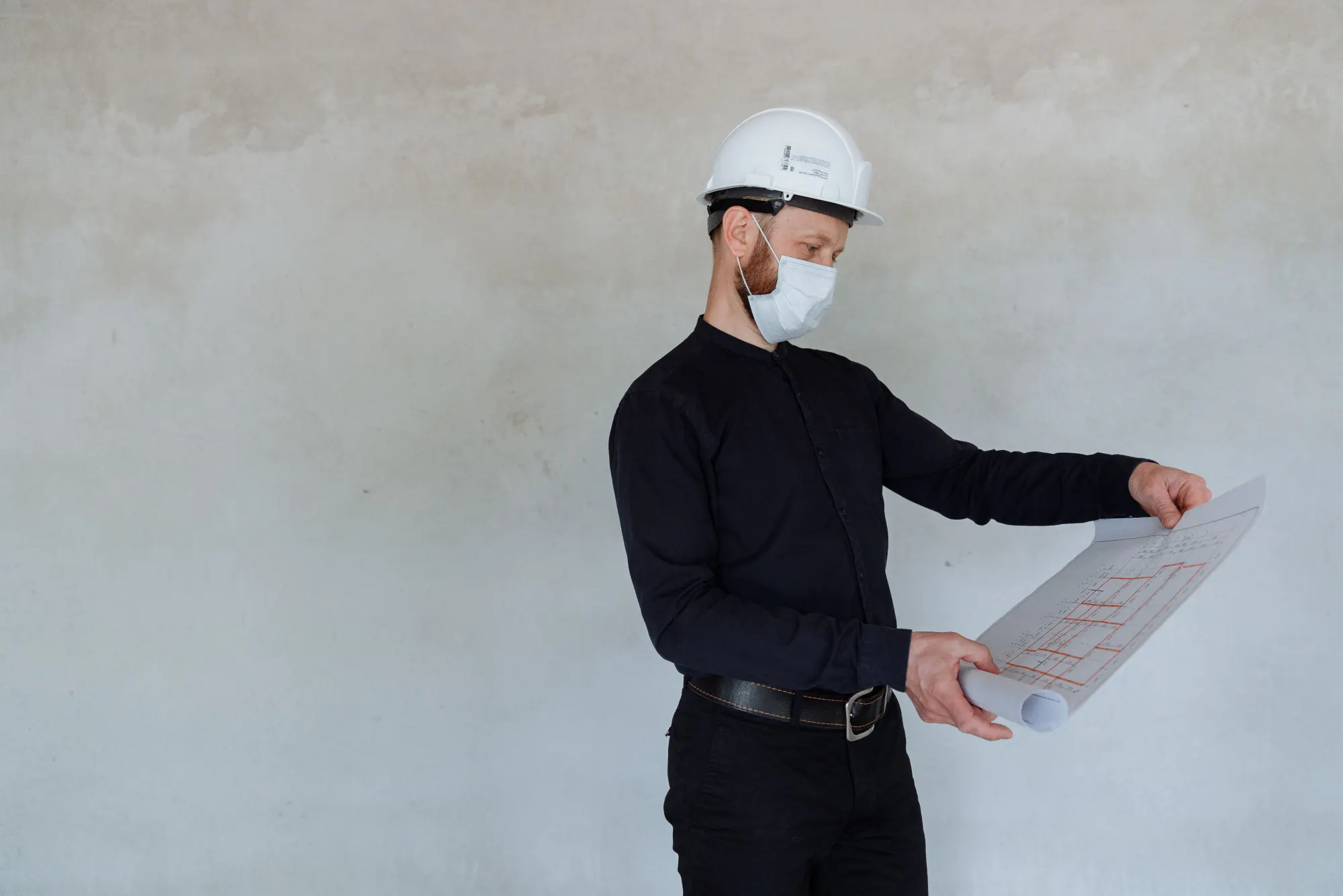 An engineer in a hard hat reviewing a blueprint against a bare wall.