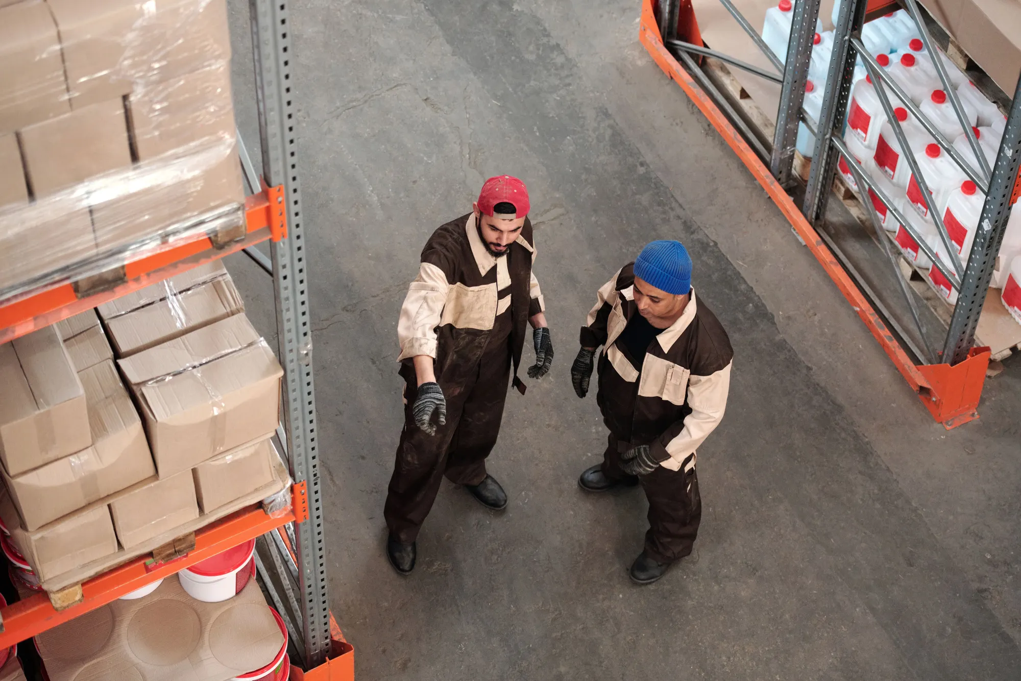 Two warehouse workers in conversation between pallet racking.