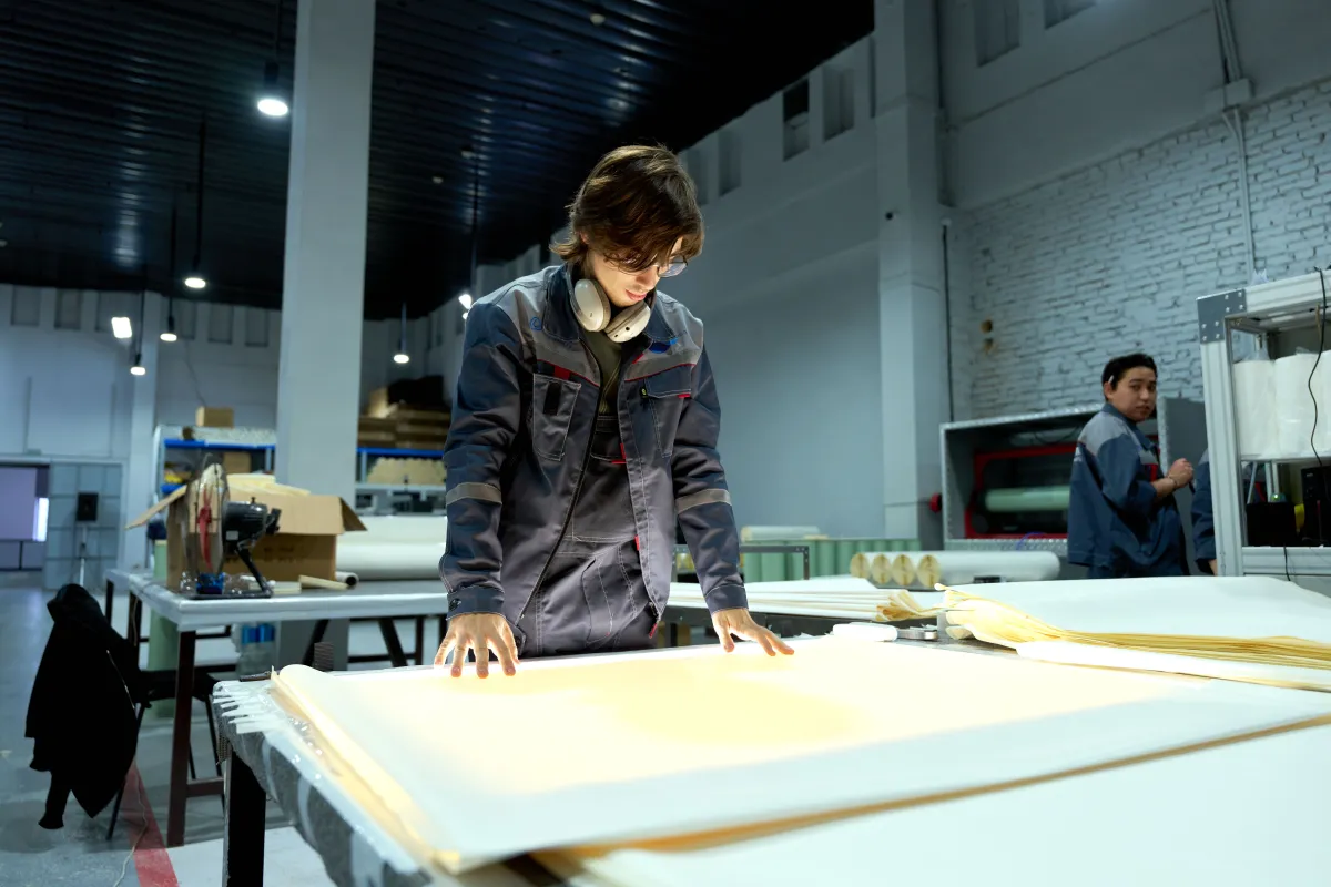 A factory worker inspecting sheet materials on a production table.