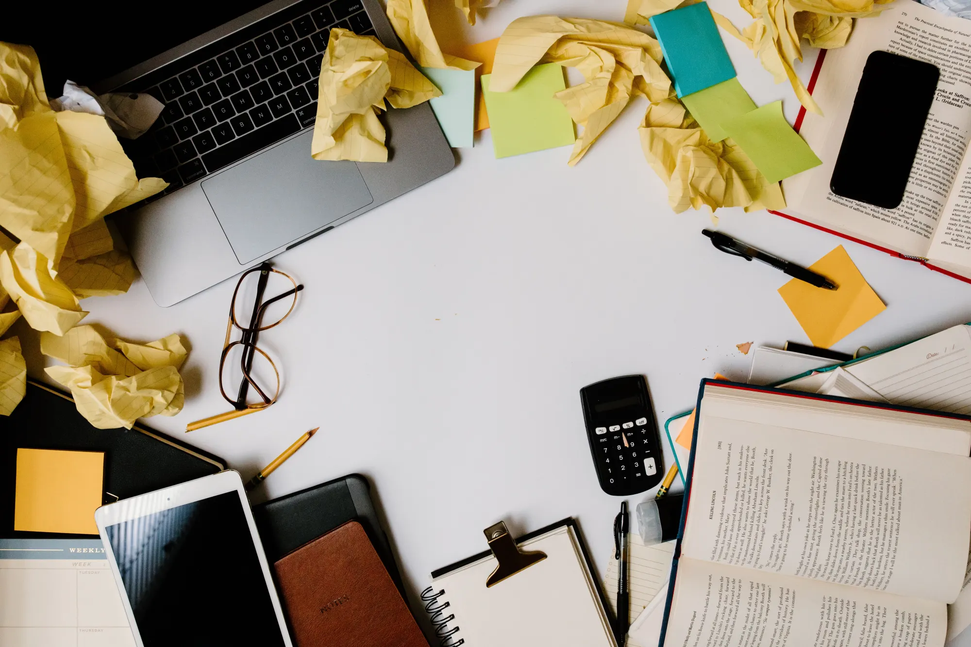 A cluttered desk with a laptop, calculator and scattered paper.