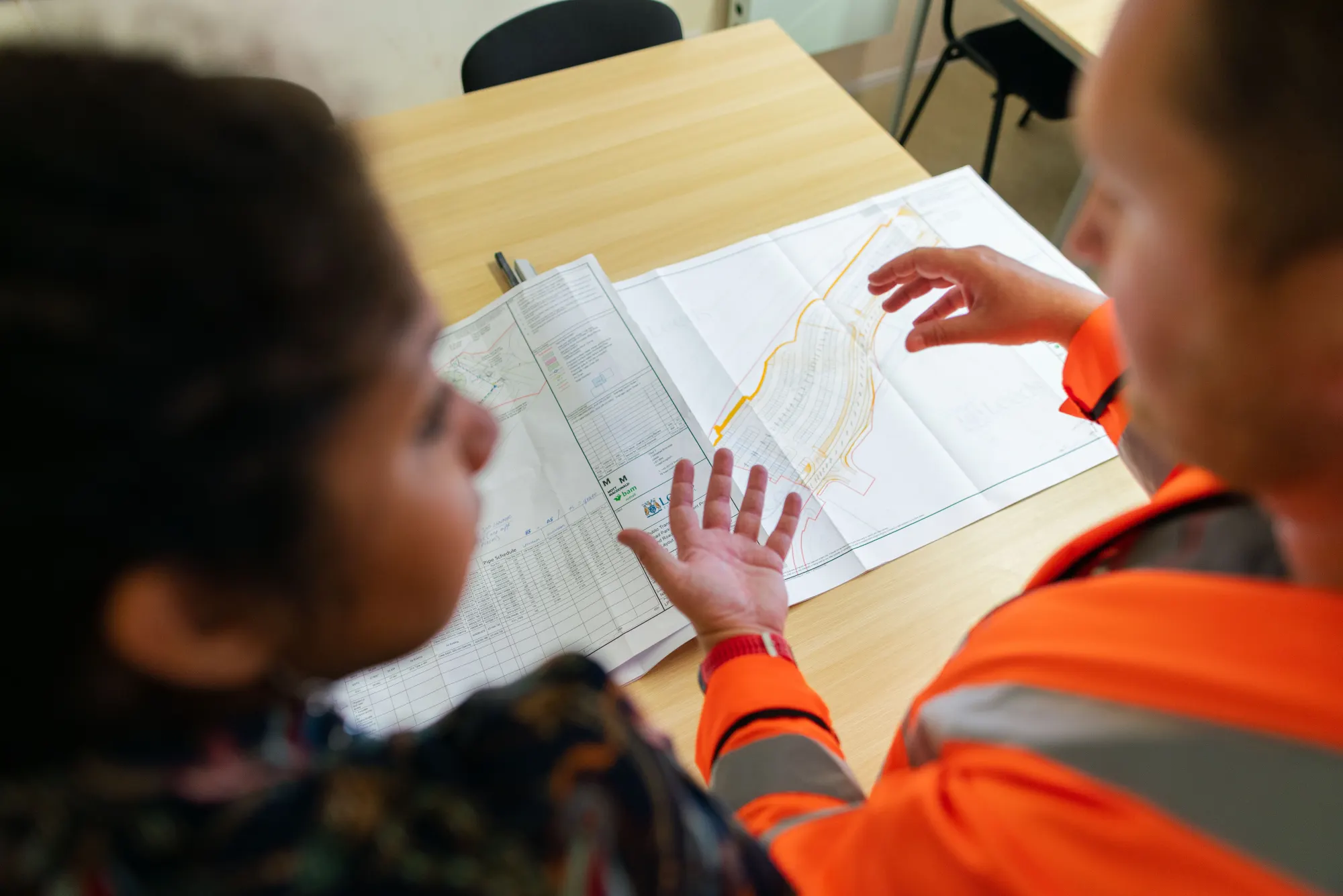 Two engineers reviewing a site plan on a desk.